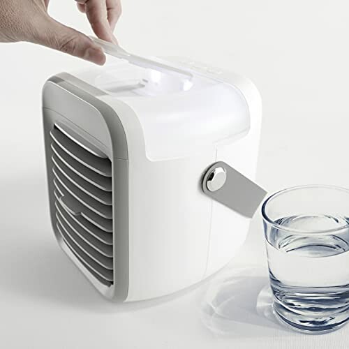 Kleine tragbare Klimaanlage neben einem Glas Wasser.